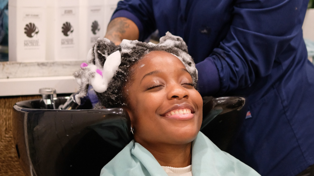 A woman getting her hair shampooed with Triple Threat Detox Shampoo at a salon bowl.