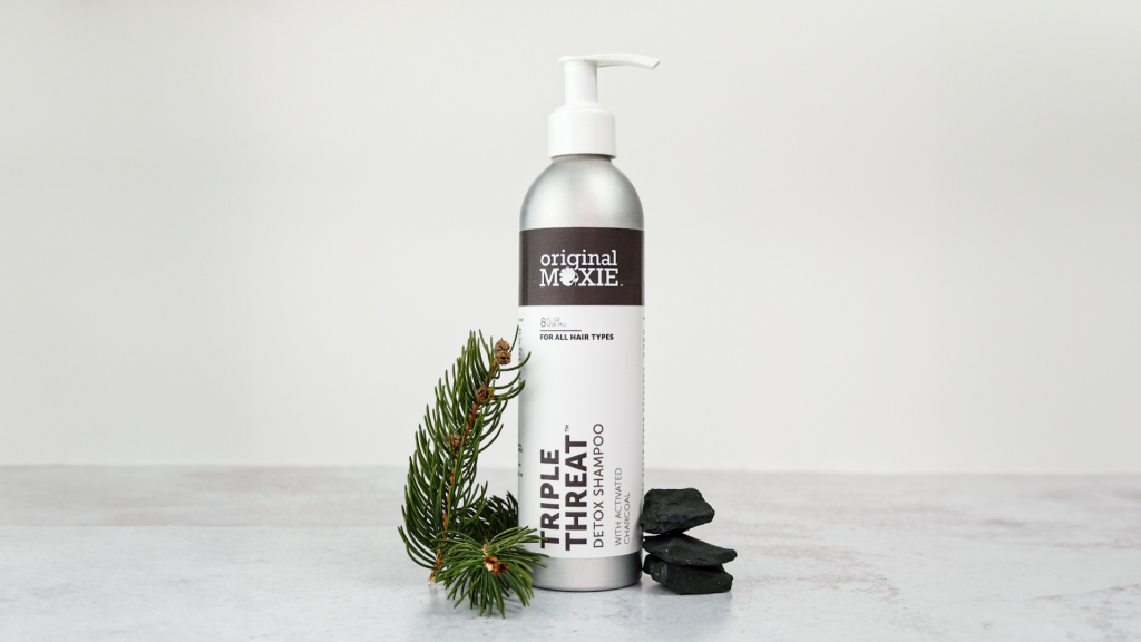 Triple Threat Detox Shampoo in an aluminum 8 ounce bottle. A sprig of fir and pieces of activated charcoal are next to the bottle.